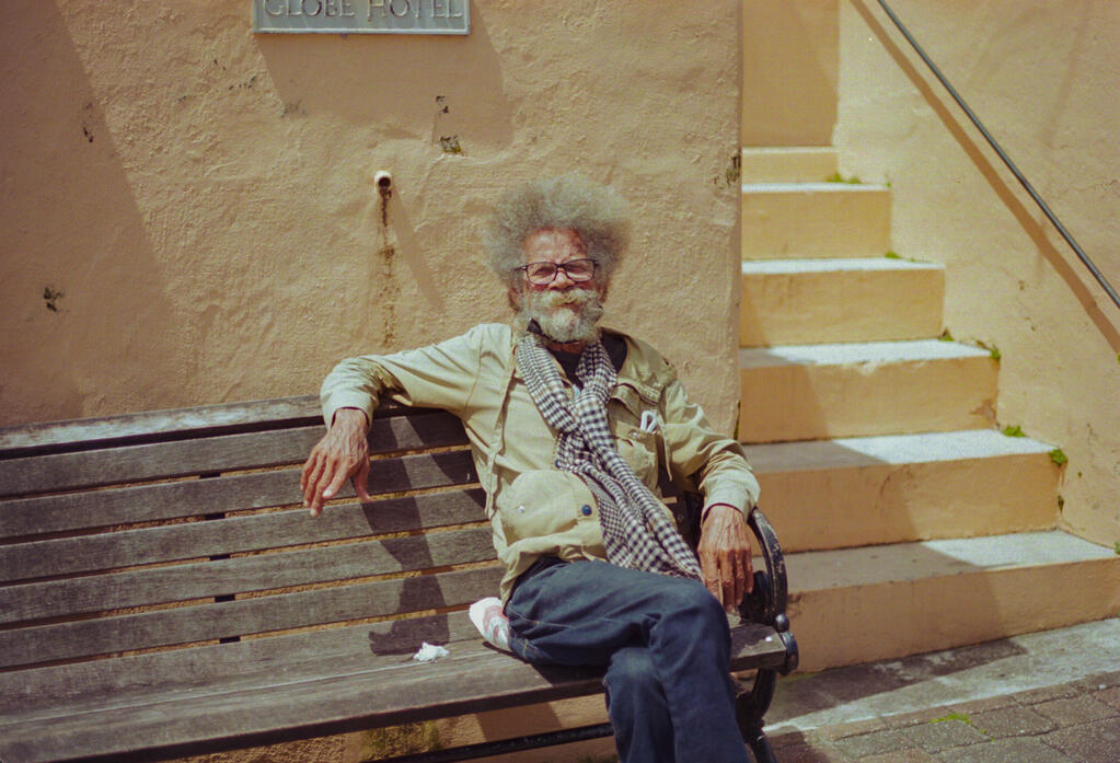 A man sitting on a park bench outside The Globe Museum in Hamilton, Bermuda. (Photo taken with subject's consent. Shot on Canon AE-1 on Kodak Portra 400 film, April 2025.)